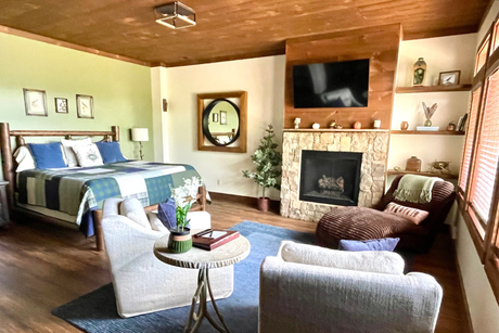 A cozy bedroom with wood paneling, a large bed, armchairs, and a blue rug.