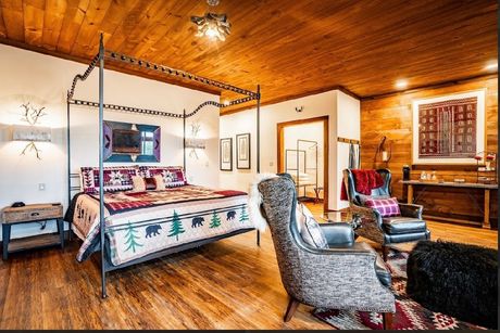 Bedroom with a four-poster bed, two leather chairs, and a side table. Burgundy and black colors dominate the decor.