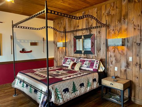 Bedroom with a four-poster bed, two leather chairs, and a side table. Burgundy and black colors dominate the decor.
