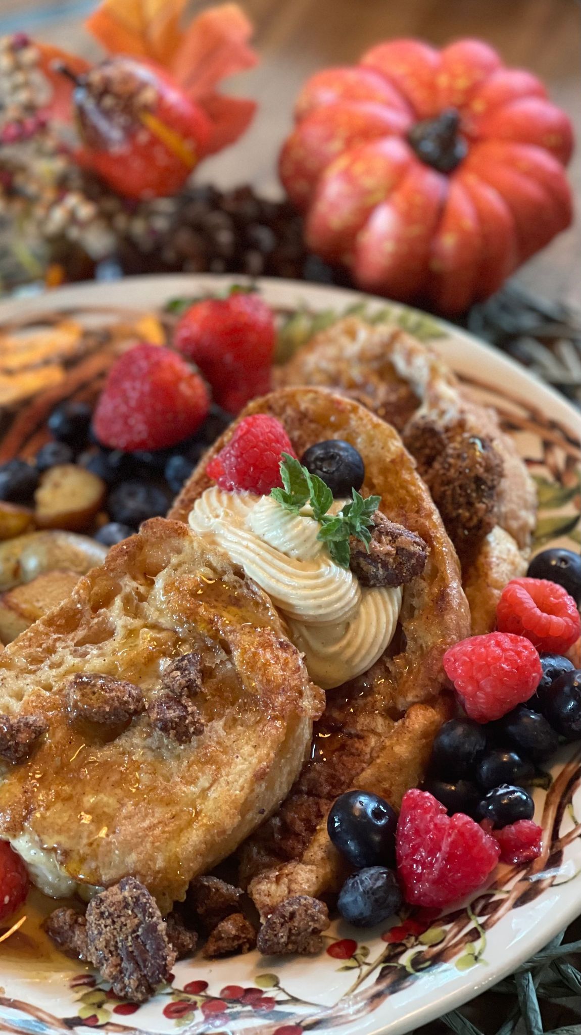 French toast with berries and cream, fall-themed plate with a pumpkin in the background.