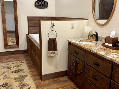 Rustic bathroom with wooden cabinetry, a built-in bathtub, and granite countertop. A wooden-framed mirror is visible.