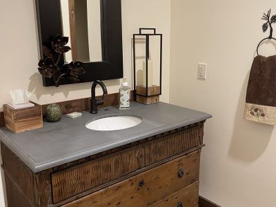 Bathroom vanity with gray countertop and wooden cabinet. Features a black faucet, mirror, and a hand towel