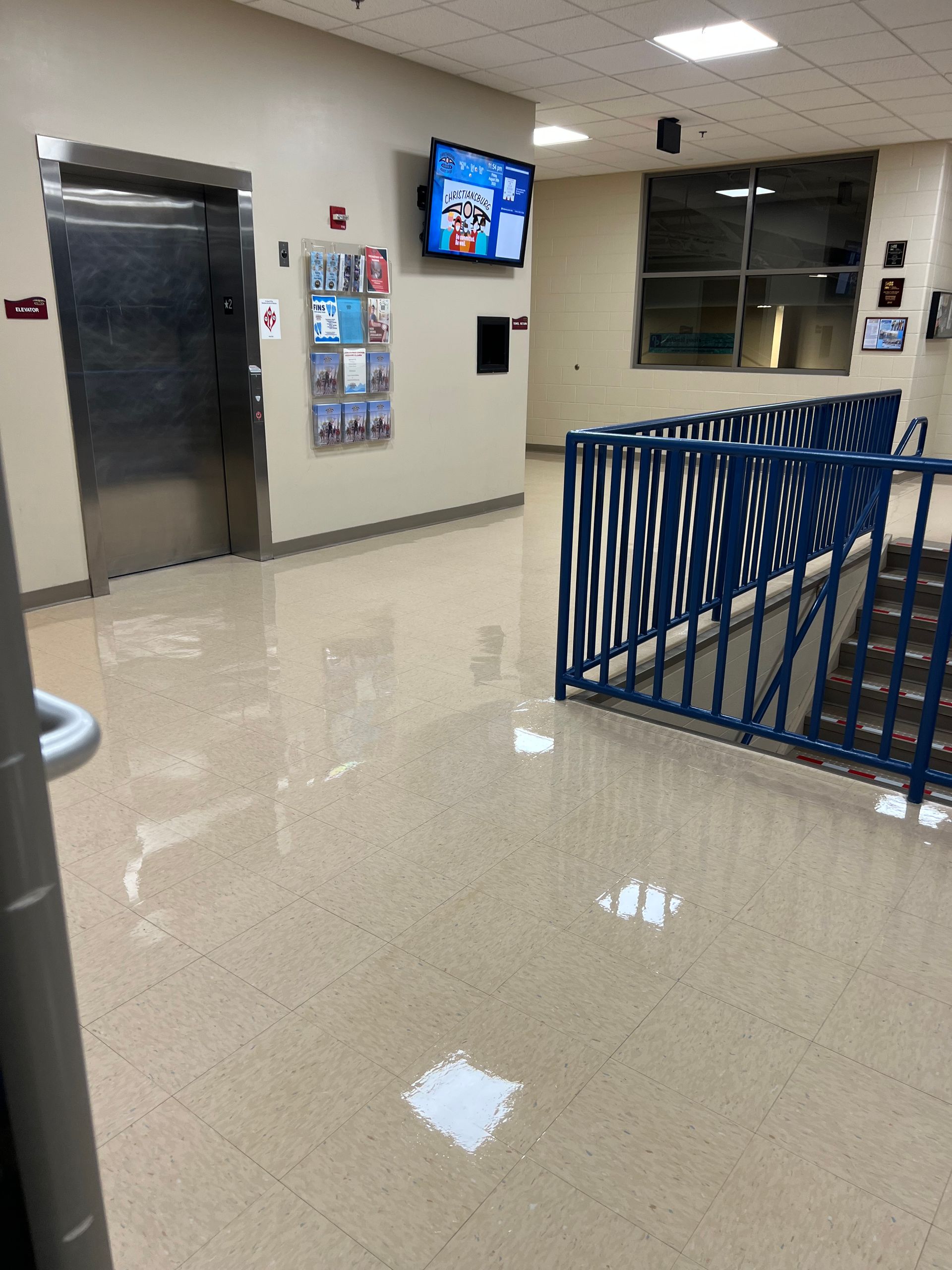 A hallway with an elevator and stairs and a tv on the wall.