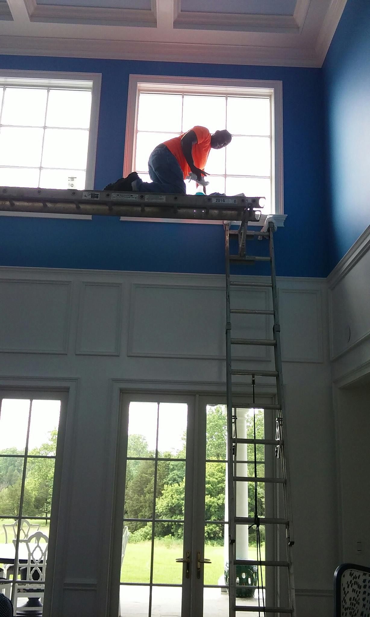 A man is kneeling on a ladder painting a window.