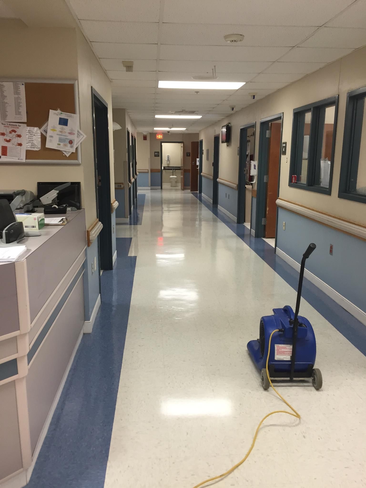 A hospital hallway with a blue vacuum cleaner on the floor.