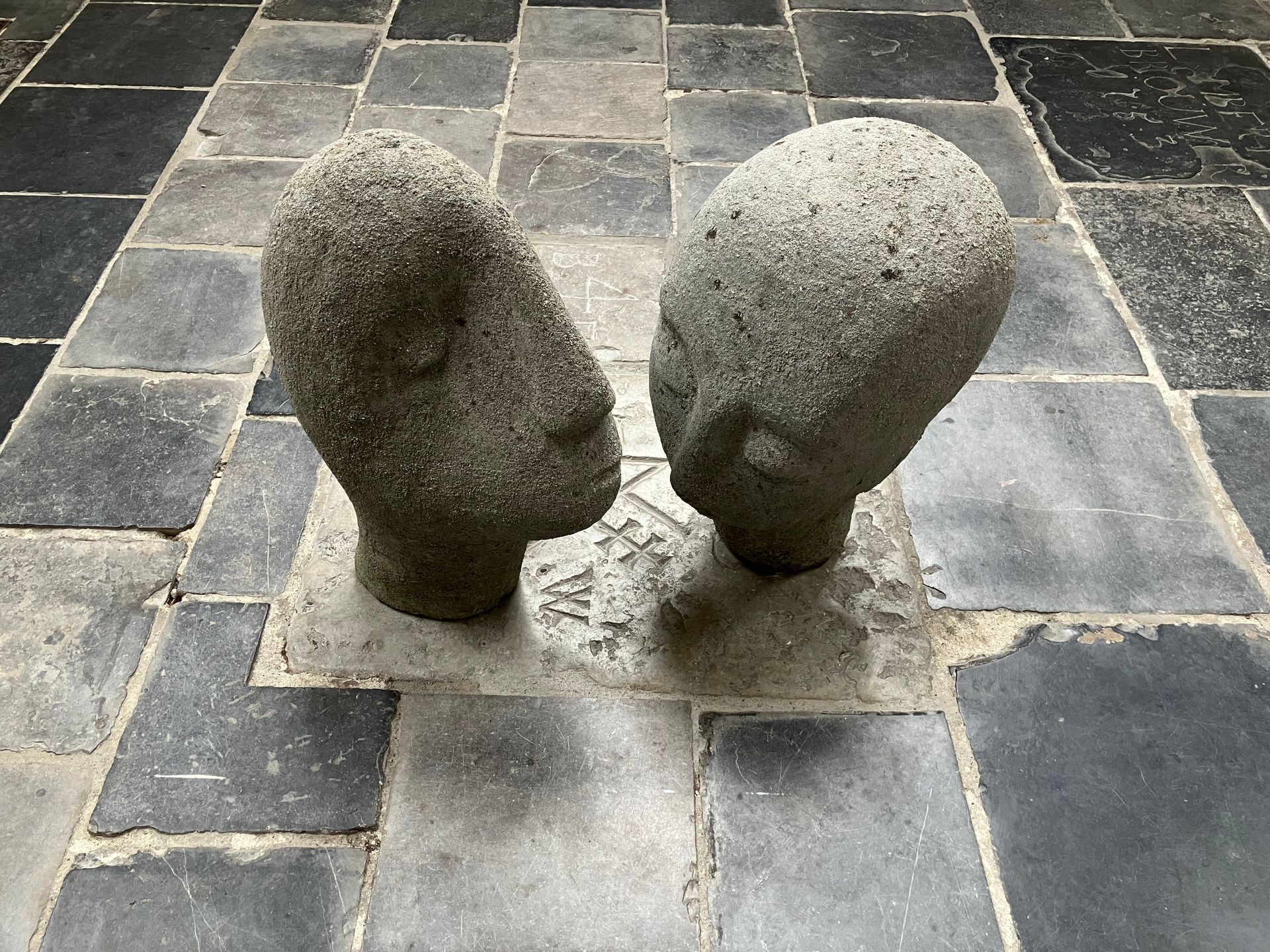 Twee stenen hoofdensculpturen op een tegelvloer. Eén hoofd is naar links gekanteld.
