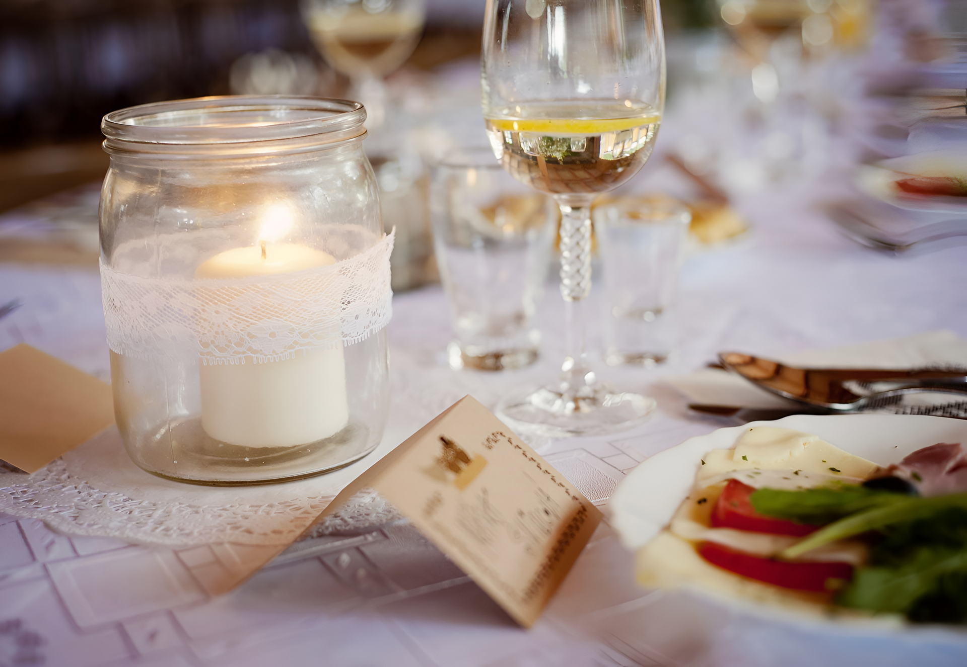 Candle in a mason jar with lace, on a table set for a formal event with food and drinks.