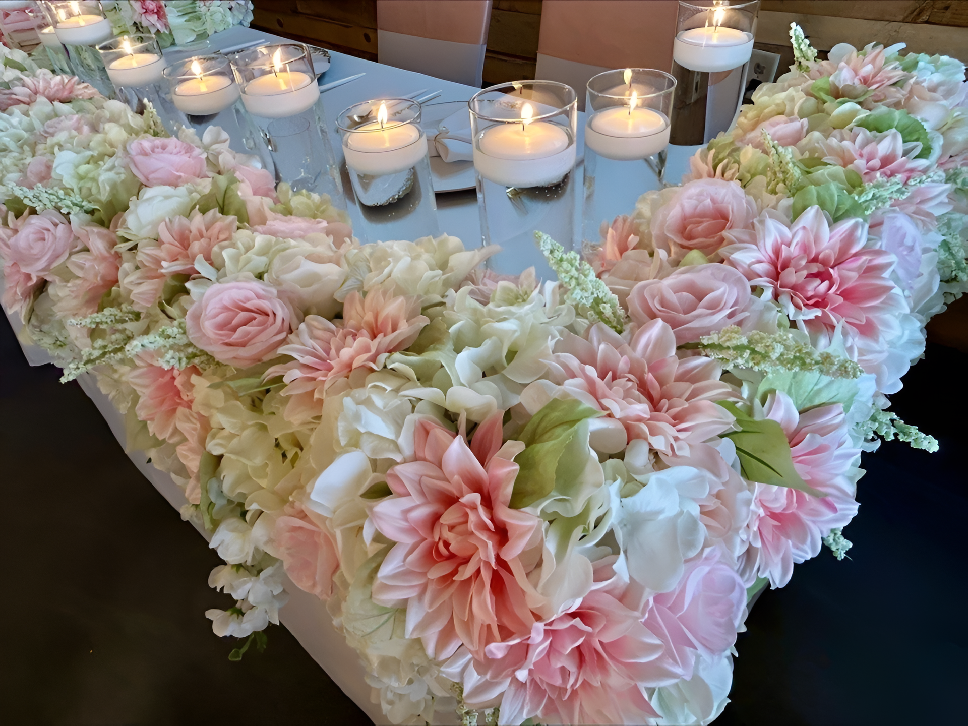 Floral centerpiece with pink and white flowers, candles on reflective surface.