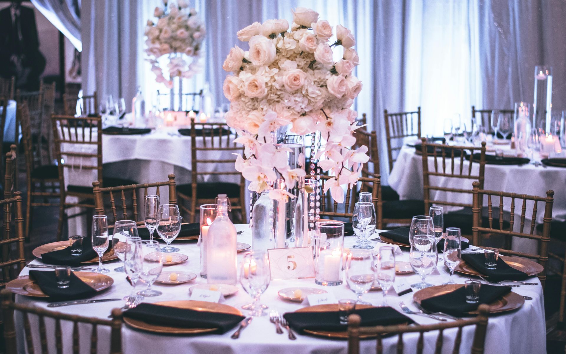 Elegant wedding reception table with white floral centerpiece, gold accents, and soft lighting.