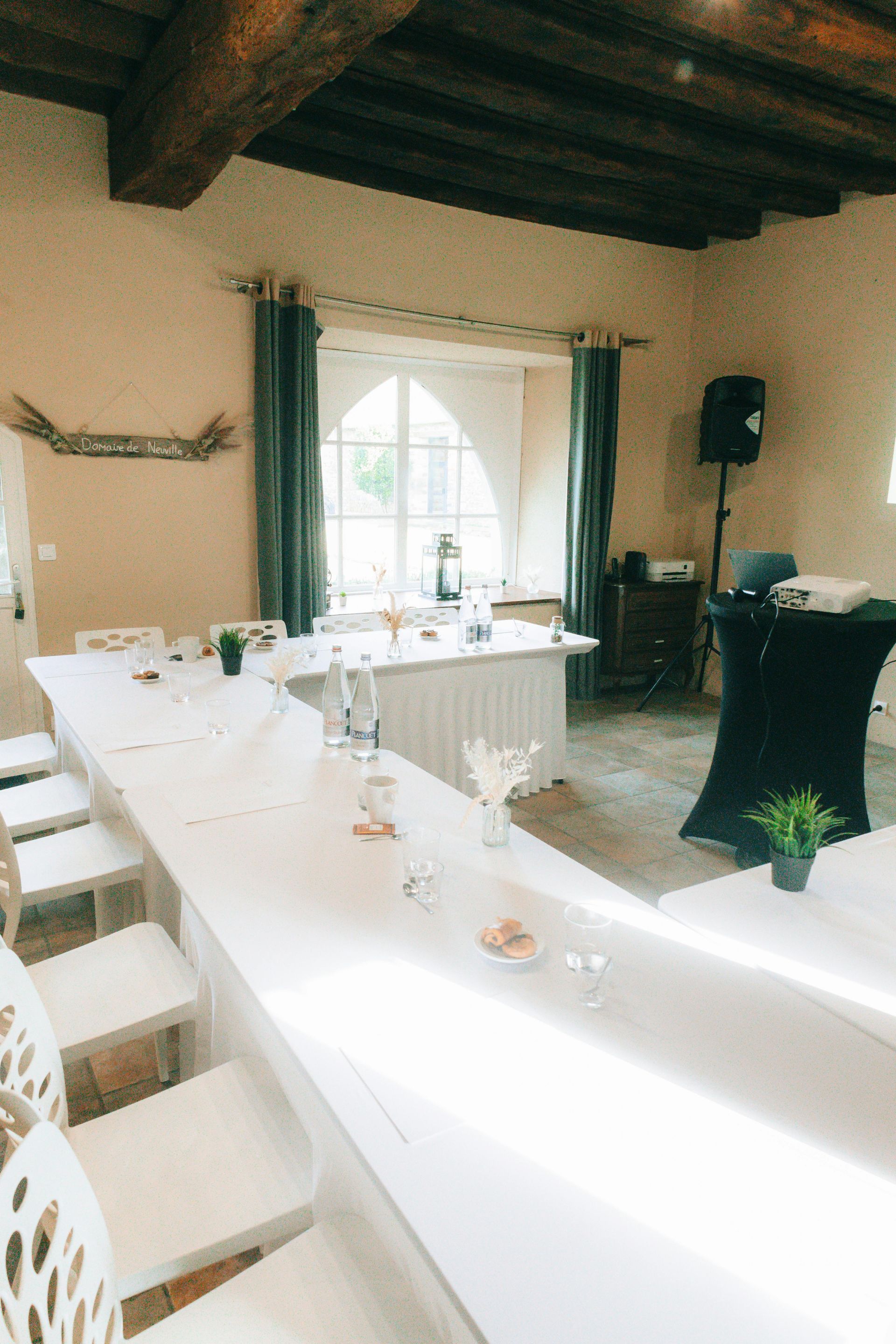 Long table set for a gathering in a room with a window, white walls, and wooden beams.