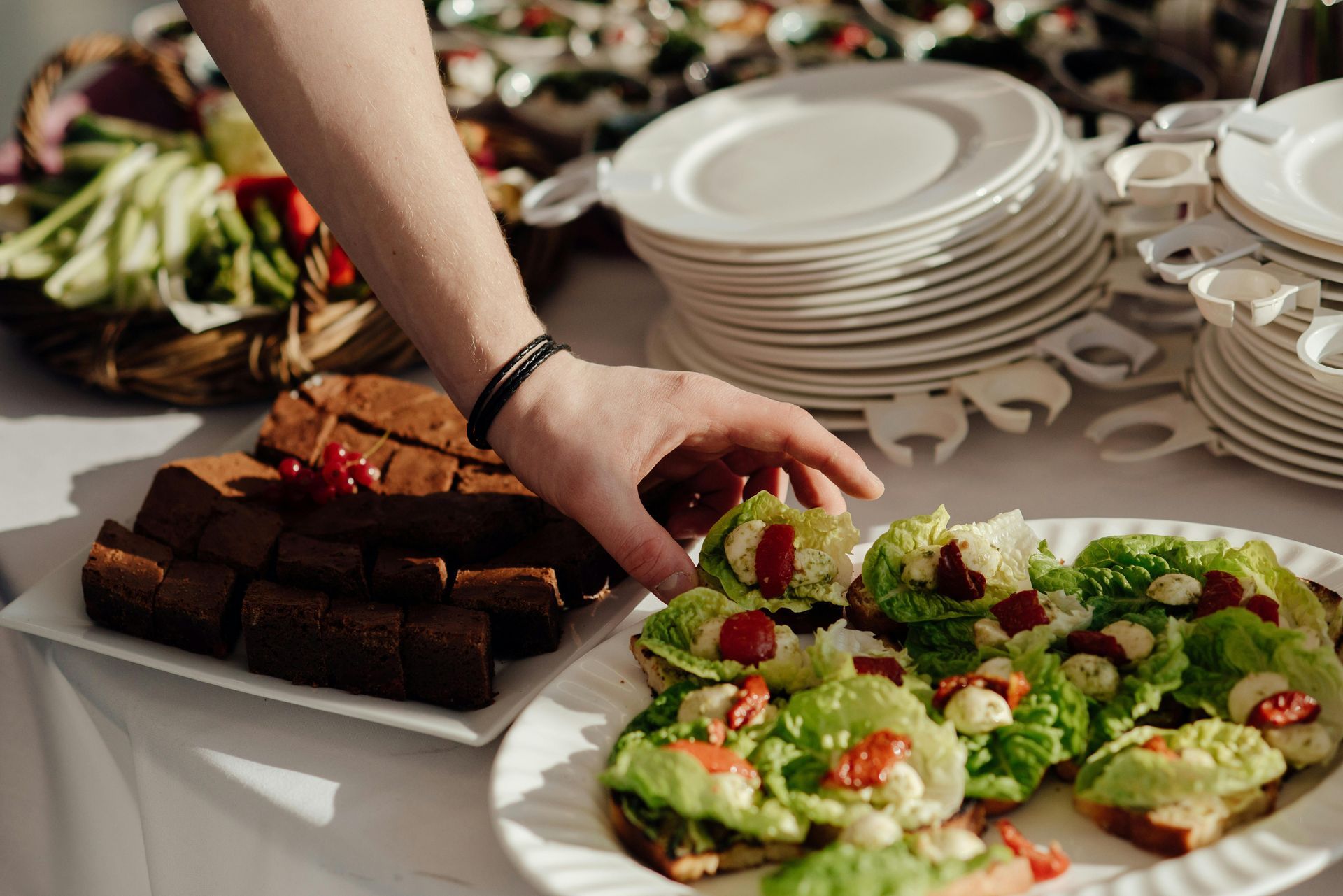 Person reaching for a bruschetta on a buffet table with brownies and plates.