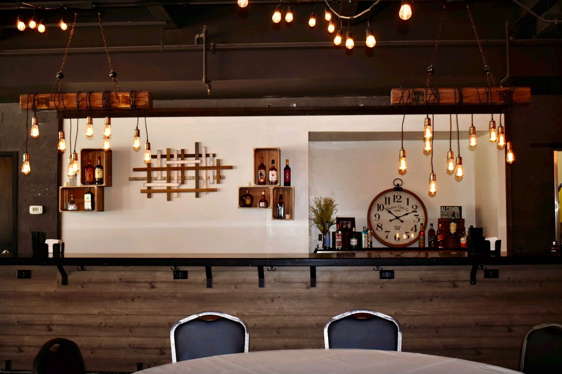 Bar with wooden accents, wine racks, and Edison bulb lights, a large clock, and seating.