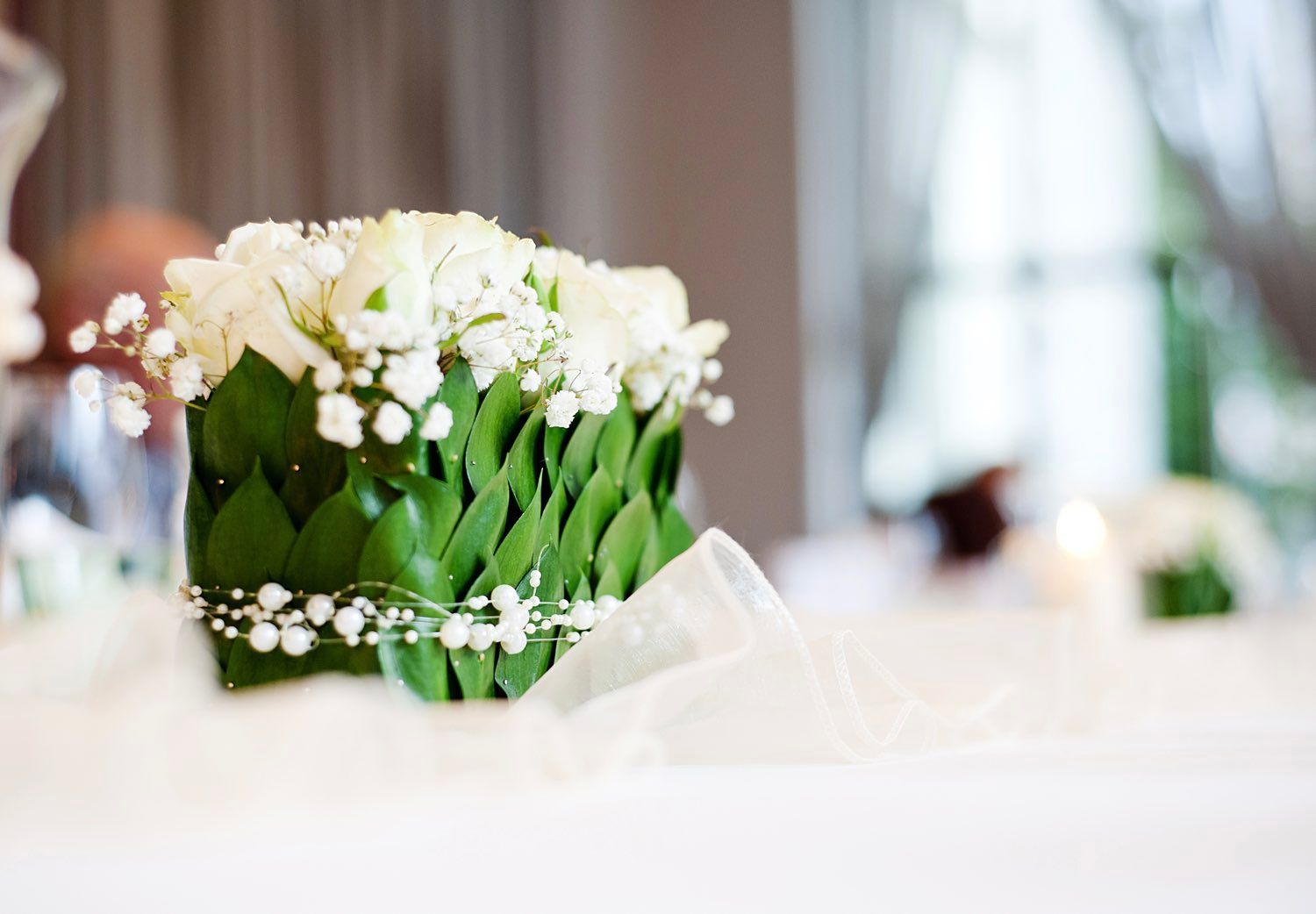 White floral arrangement with green leaf accents, on a white tablecloth.