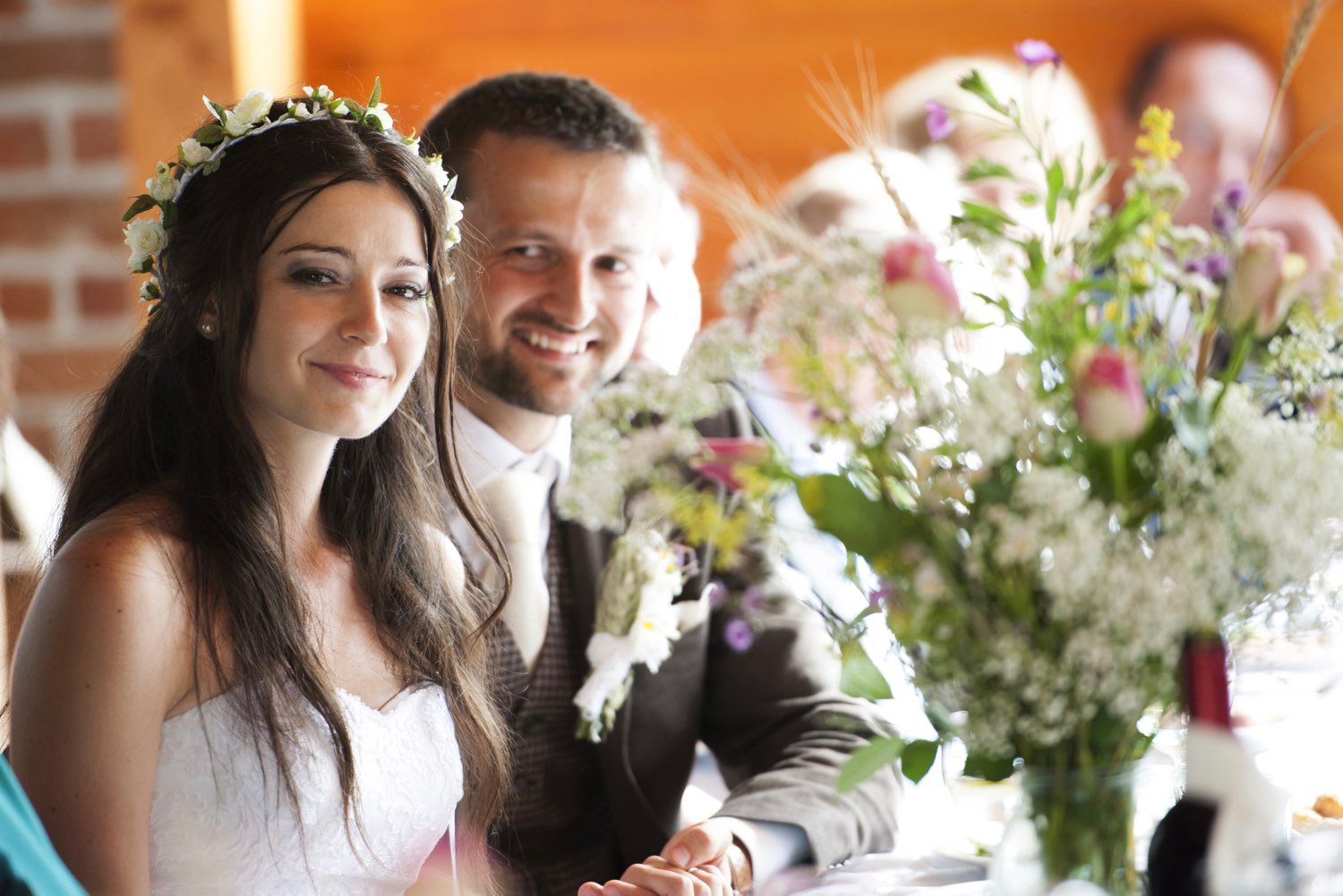 Bride and groom smiling at reception table with floral centerpiece.
