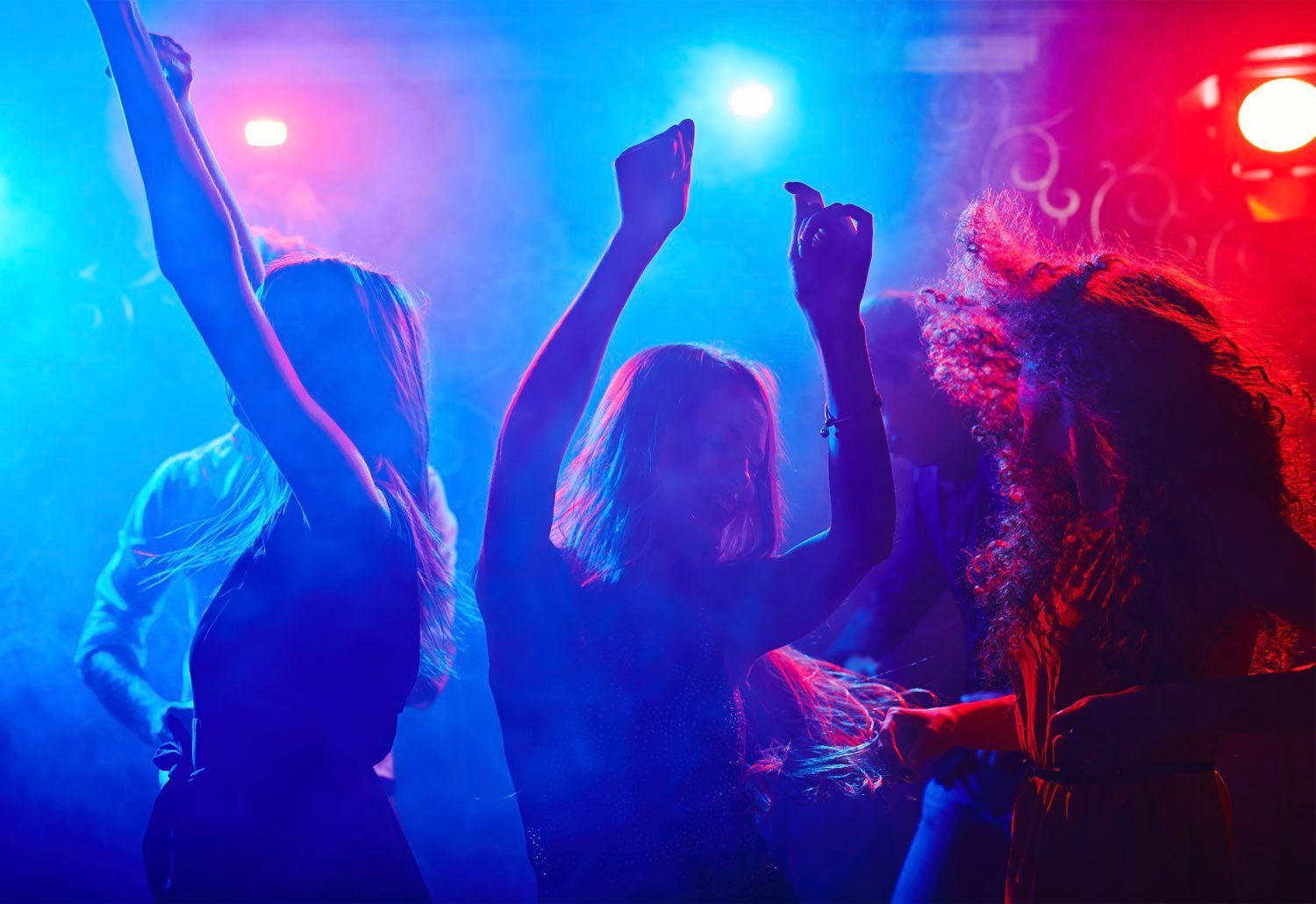 People dancing in a nightclub, illuminated by blue and red lights, arms raised.