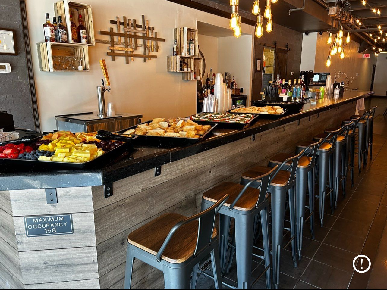 A bar with snacks, stools, and a wooden facade, illuminated by overhead lights.