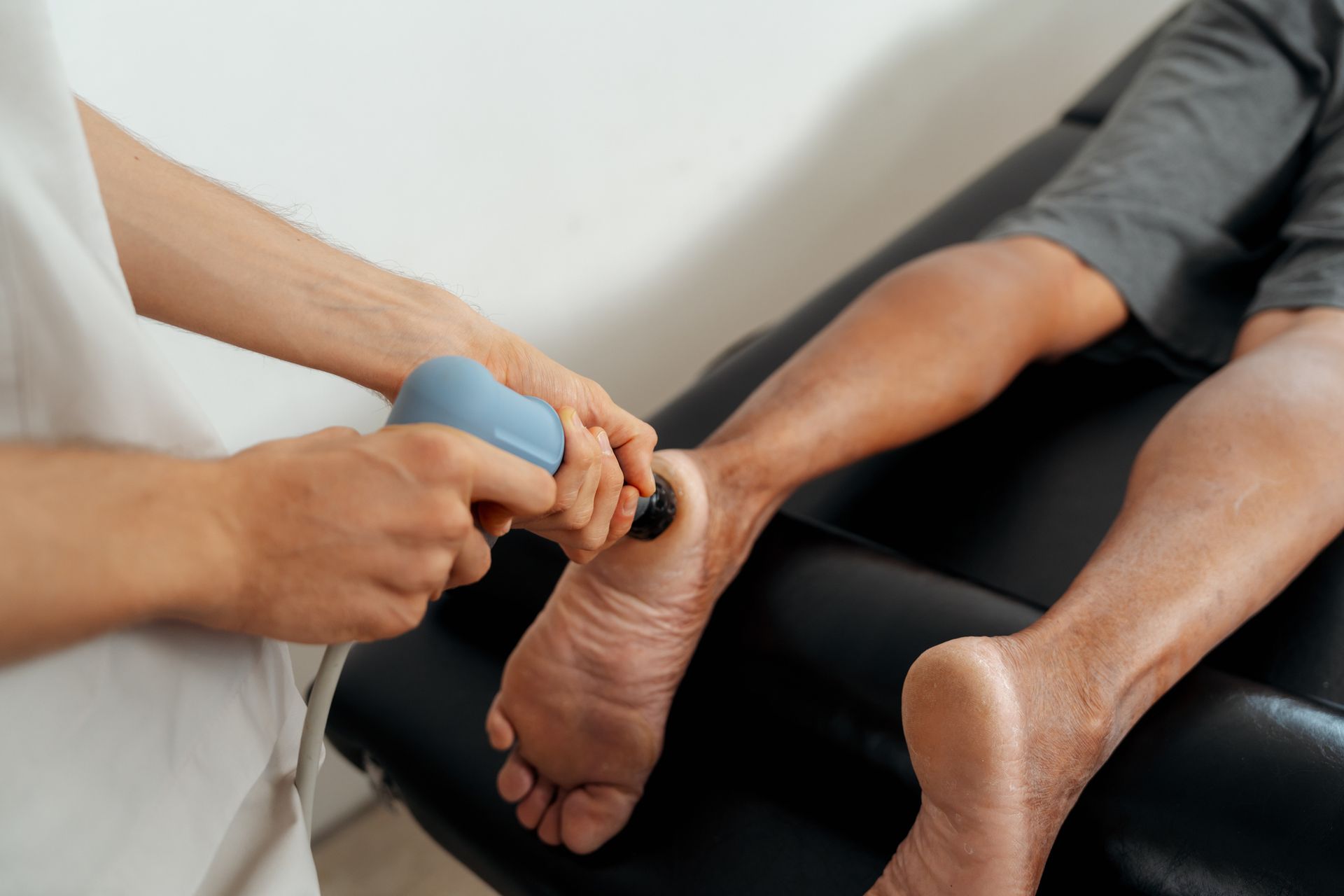 Physical therapist using shockwave therapy on patient's foot.