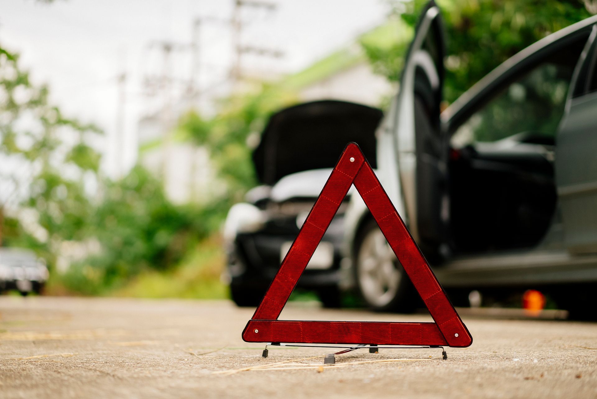 Red warning triangle on road with broken-down car, hood open and door ajar.