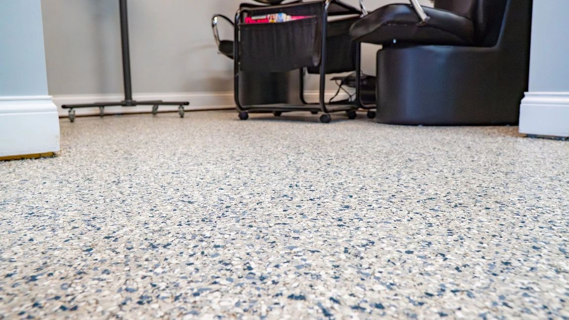A low-angle view of a speckled, gray-and-white epoxy floor in a room with a rolling cart and a chair base.