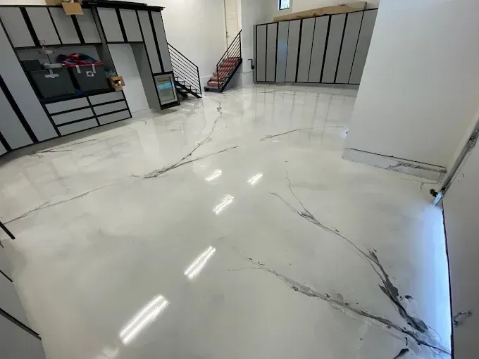 A modern garage with white and grey marble-patterned epoxy flooring, custom cabinetry, and a metal staircase.