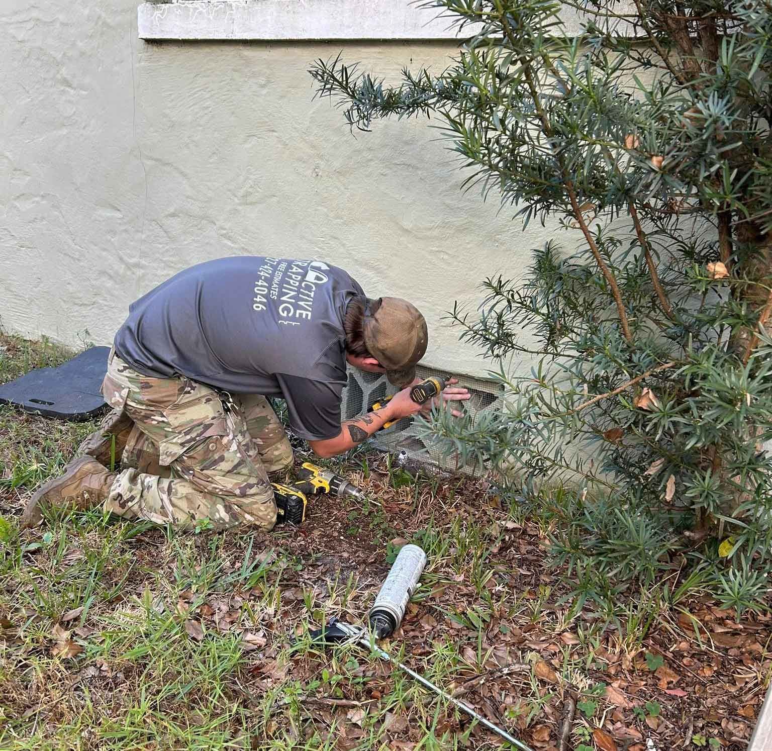Person kneeling near a wall, working with tools. Grass and small tree are in the scene.