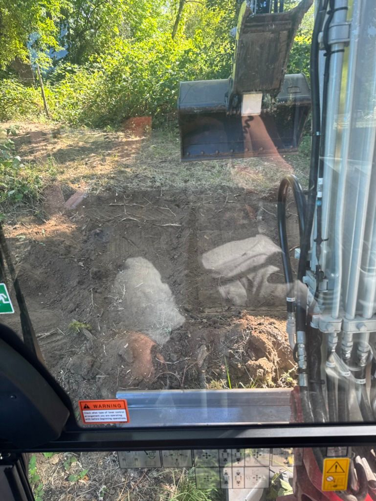 An excavator digging in a wooded area, viewed from inside the cab.