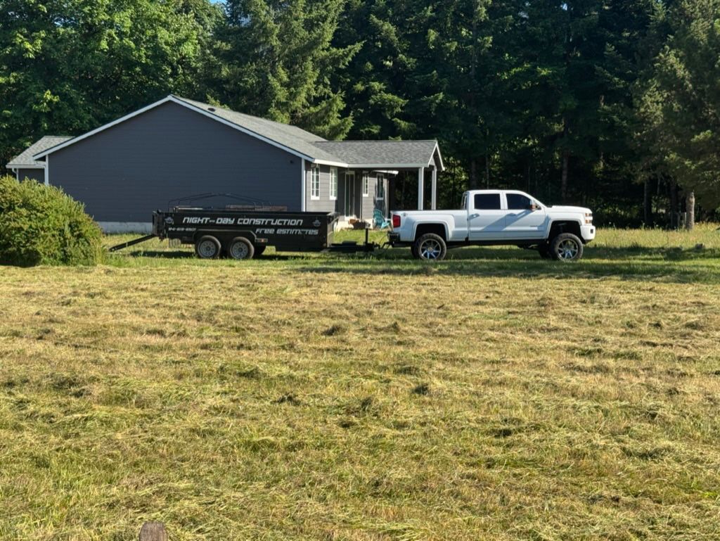 White pickup truck towing a trailer in front of a dark grey house in a grassy field.