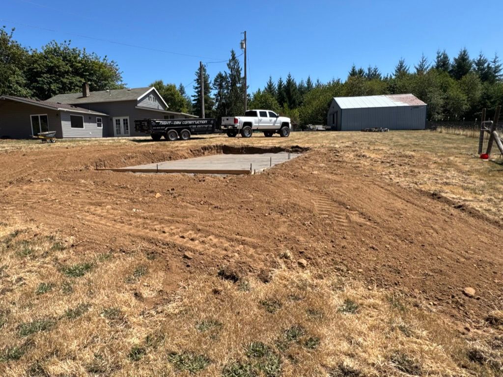 Construction site with a concrete foundation, truck, and shed in a rural area.