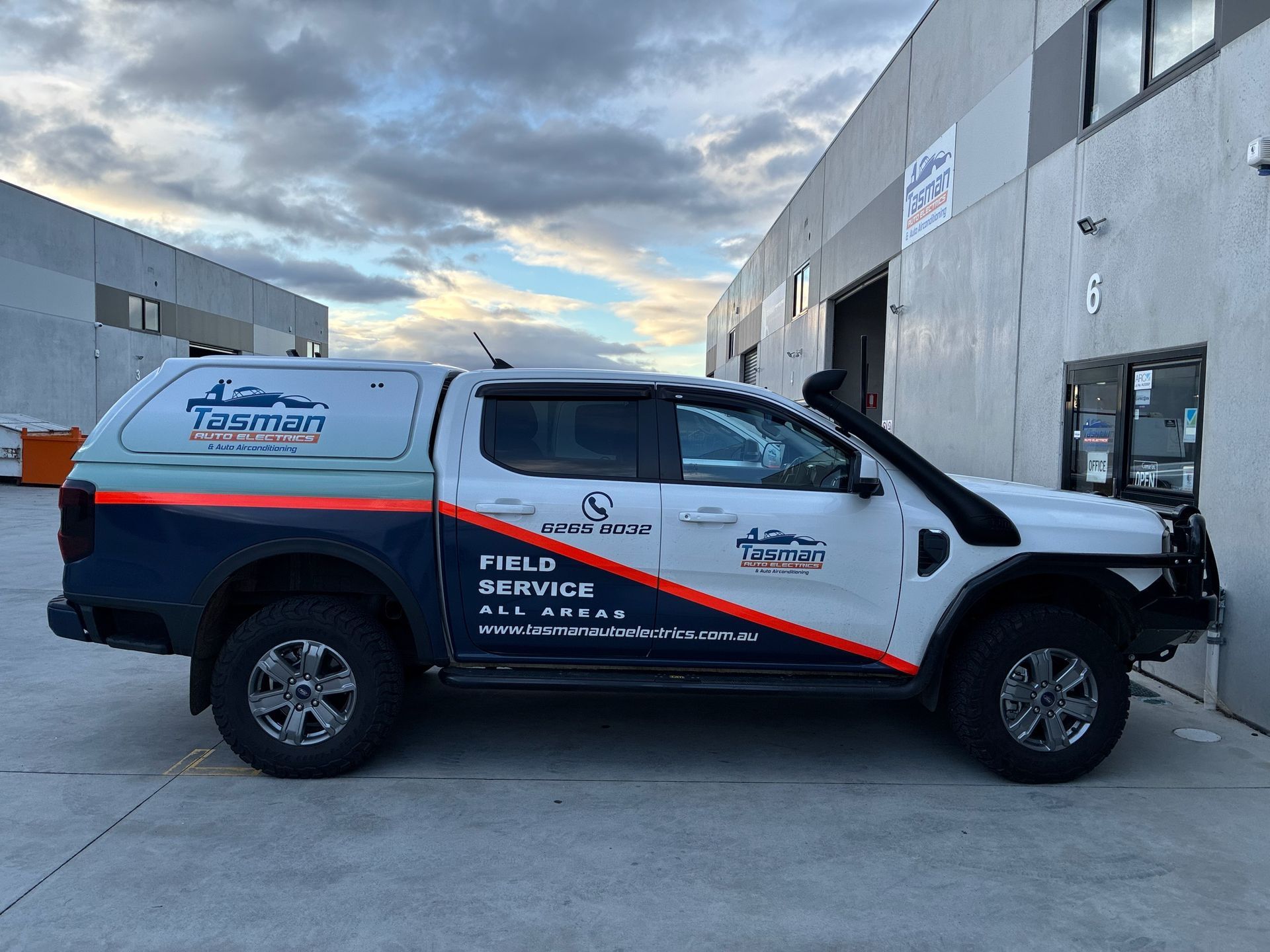 White field service truck with blue and orange stripes parked outside a building.