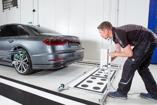 Auto electrician calibrating vehicle sensors in workshop.