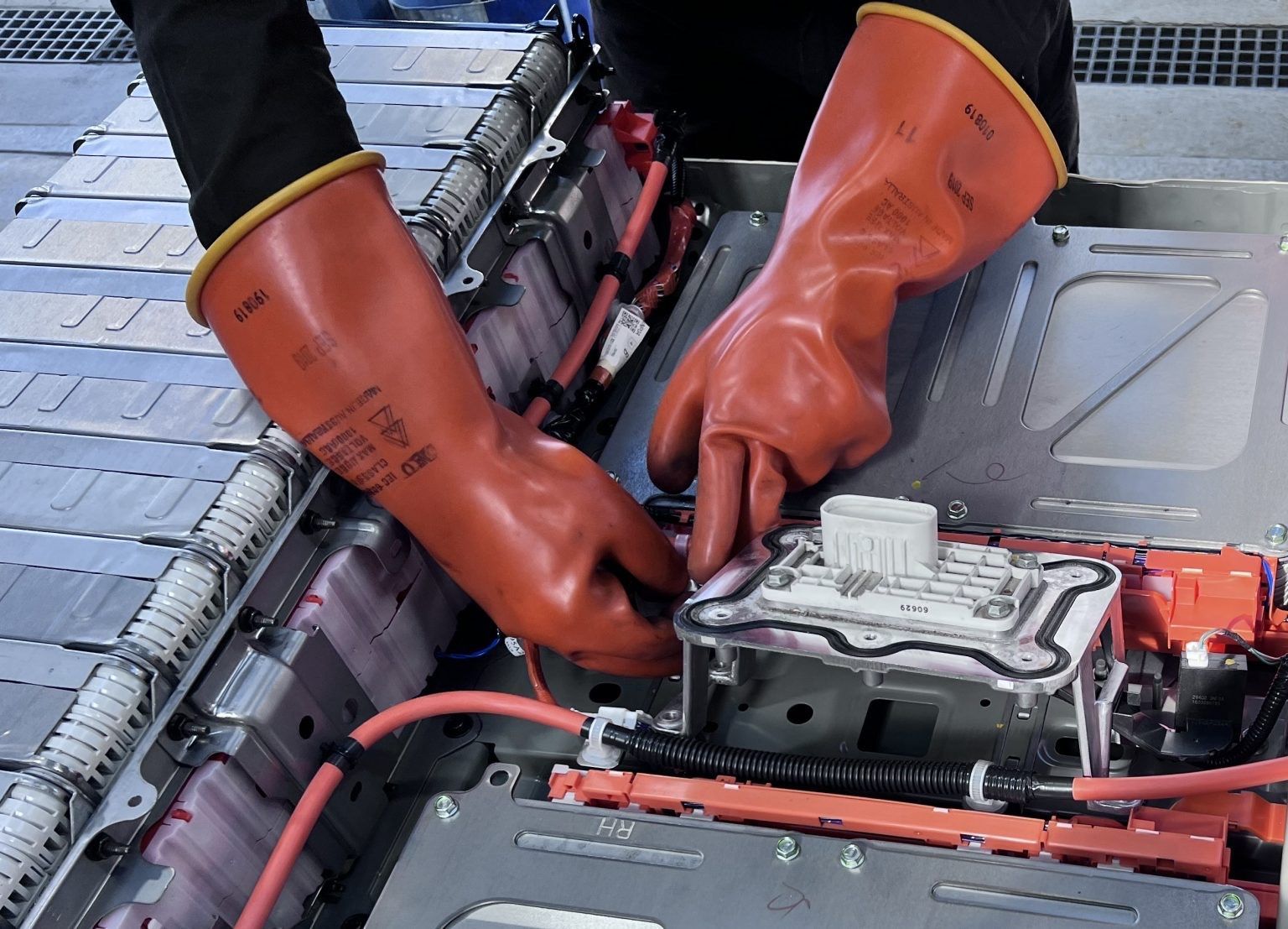 Hands in orange gloves assembling EV battery components.