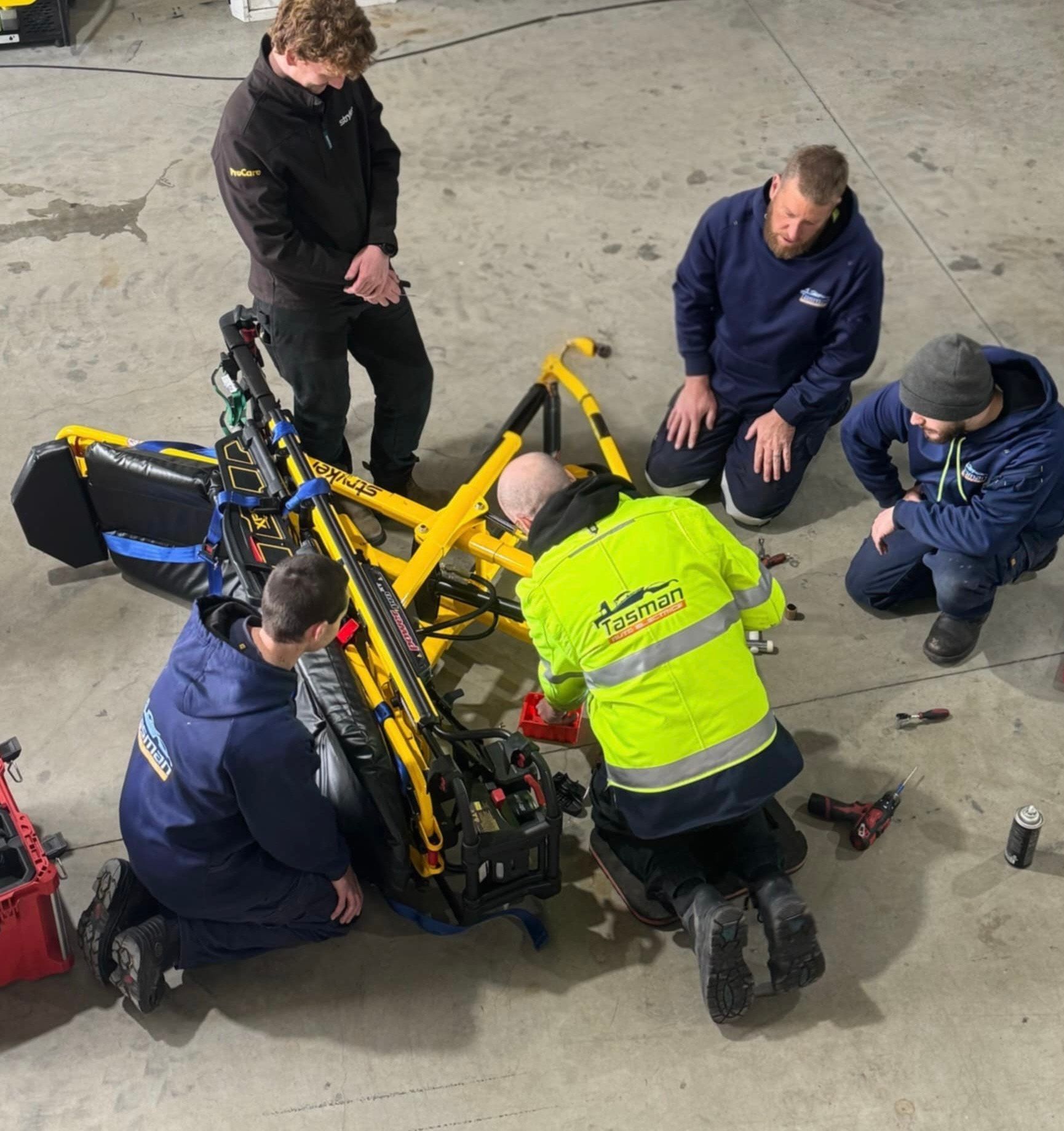 Five people working on a yellow and black medical device on a concrete floor.
