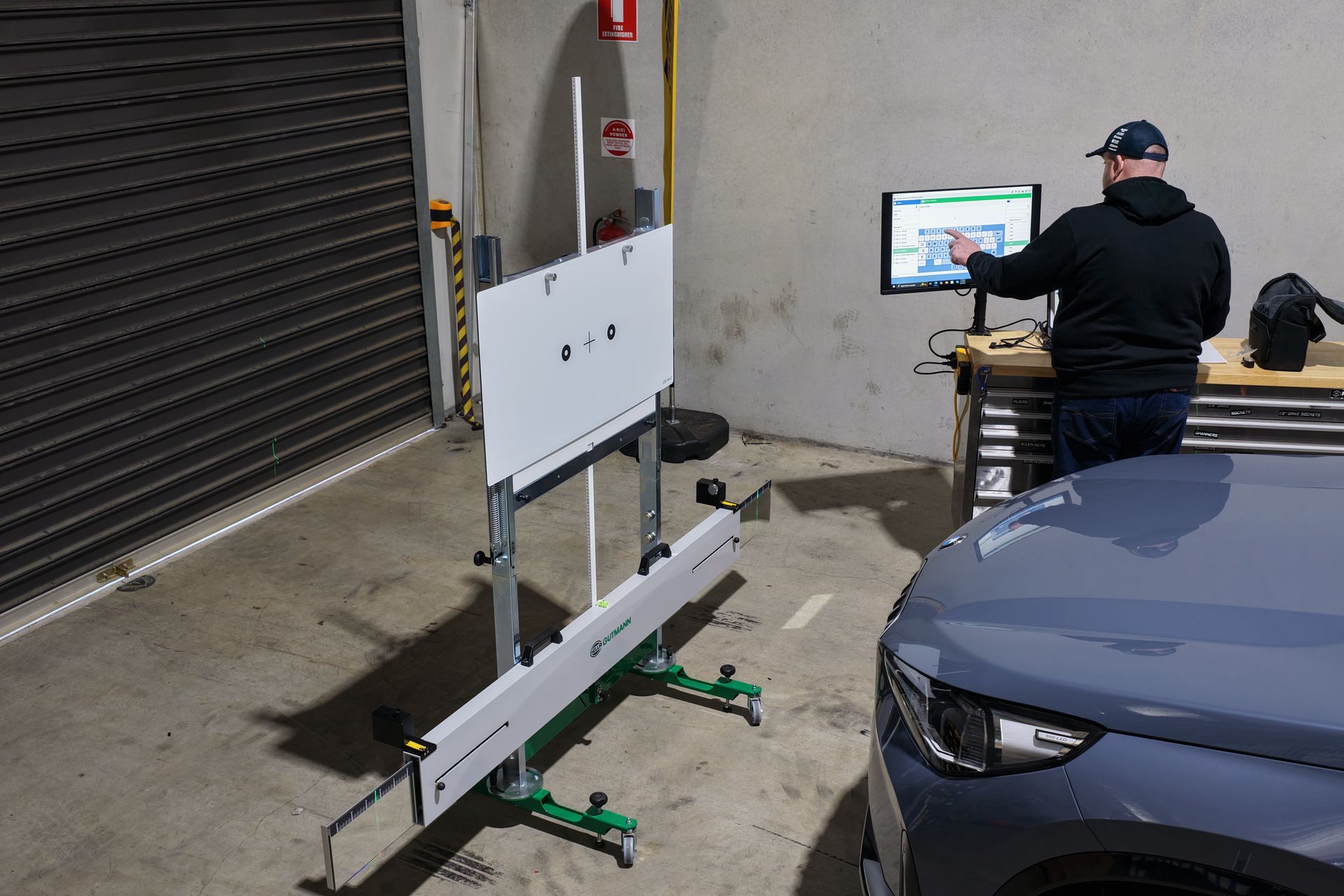 Man using computer to align a car, with alignment equipment set up in a garage.