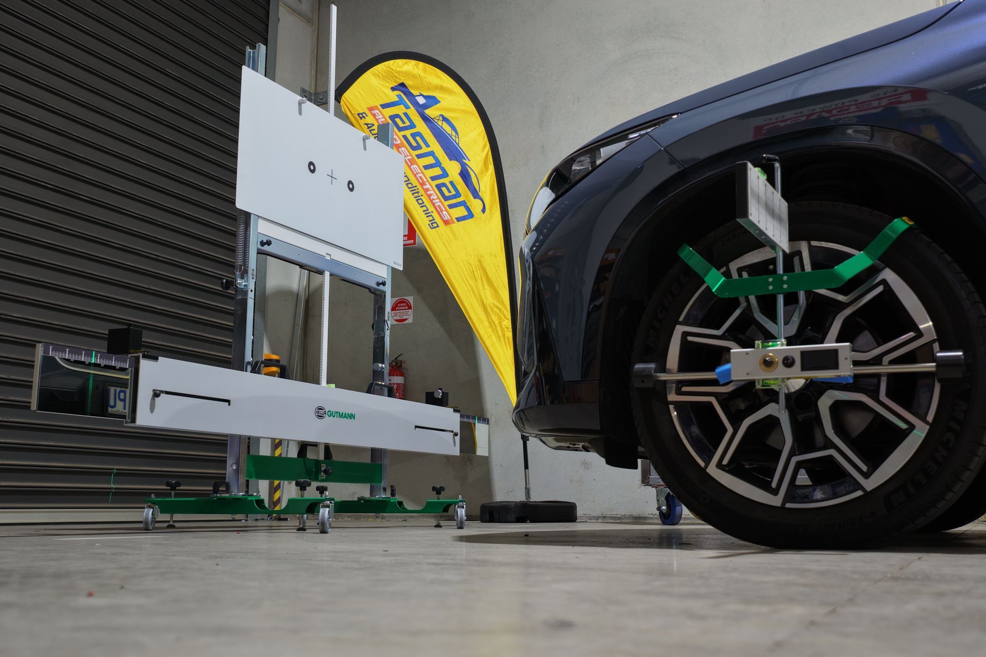 Car wheel alignment machine on a blue car's front wheel in a garage.