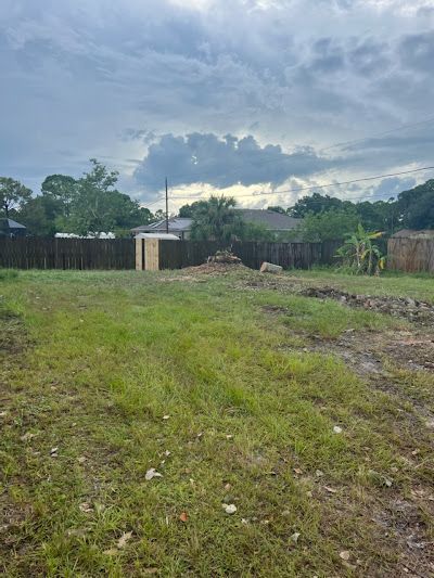 A large grassy field with a house in the background and a cloudy sky.