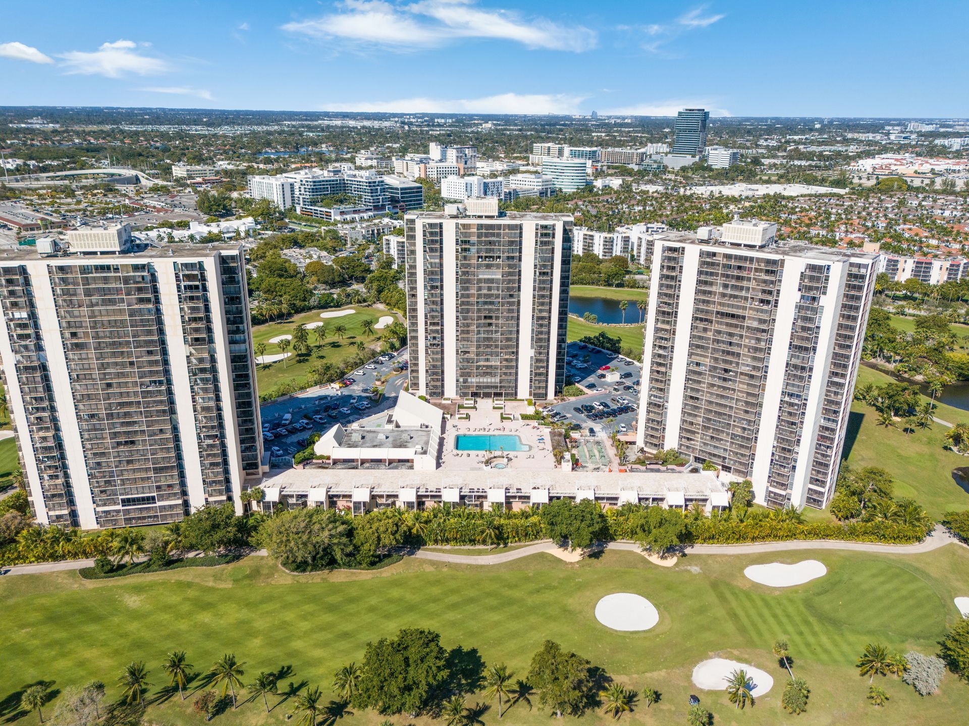 An aerial view of three high-rise apartment buildings surrounding a central pool on a golf course.