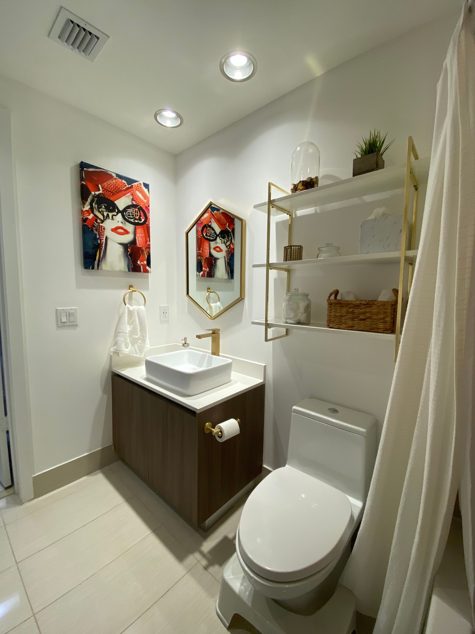 A modern bathroom with a wood vanity, white square sink, gold-framed mirror, floating shelves, and a white toilet.