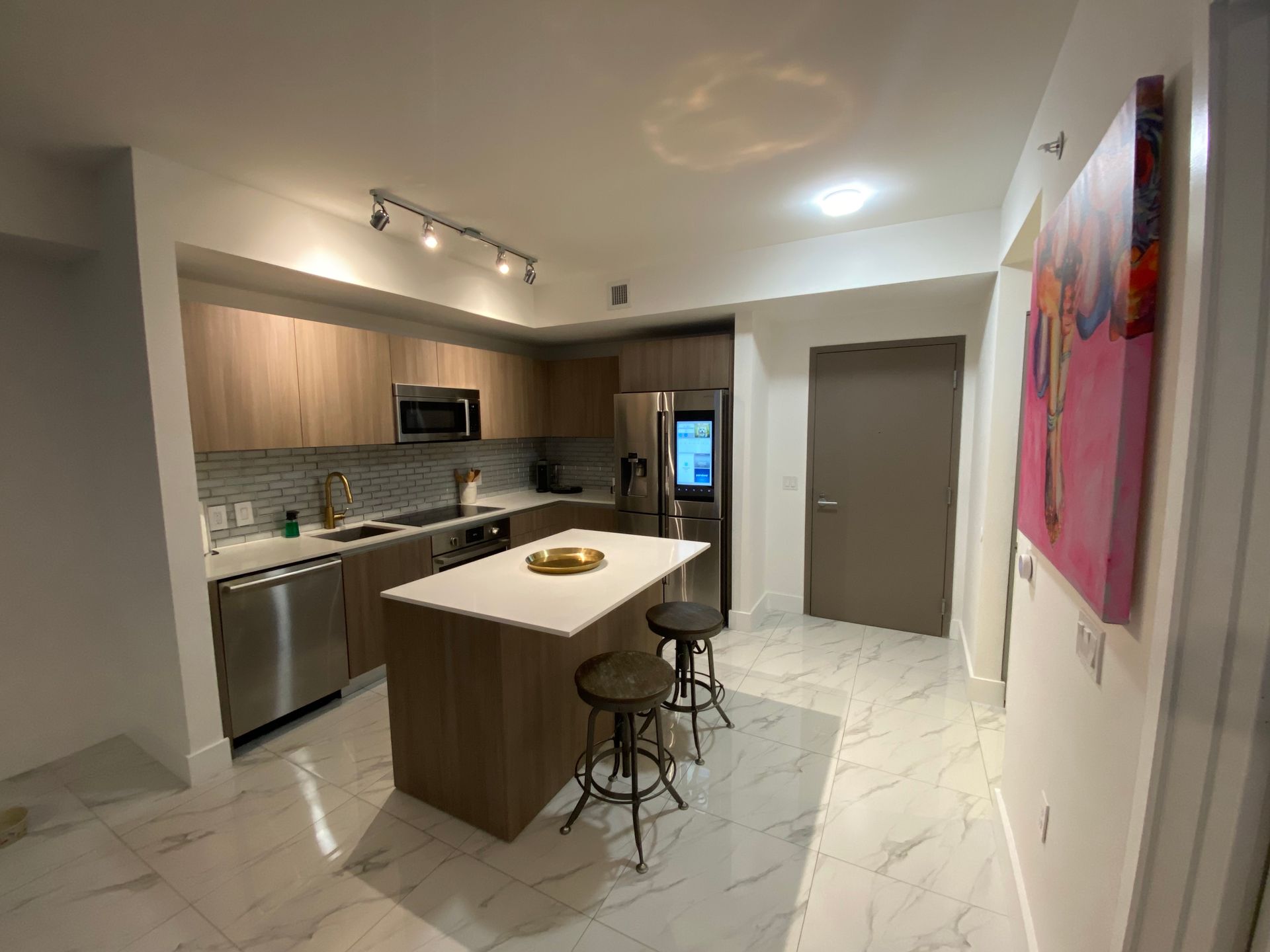 A modern kitchen with light wood cabinets, a white island, stainless appliances, and marble-look tile flooring.