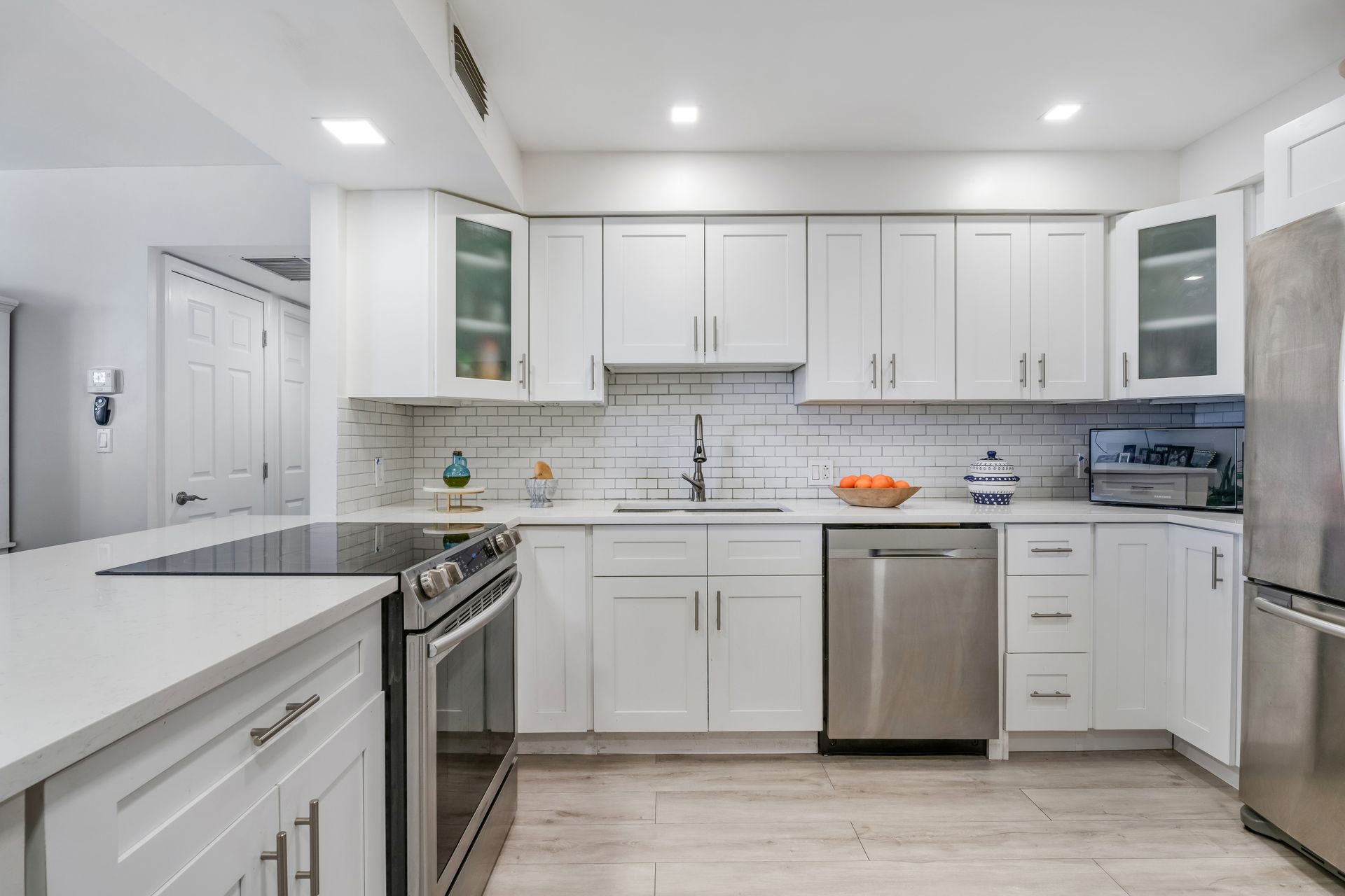 A modern, well-lit kitchen with white shaker cabinets, stainless steel appliances, and a light-colored quartz countertop.