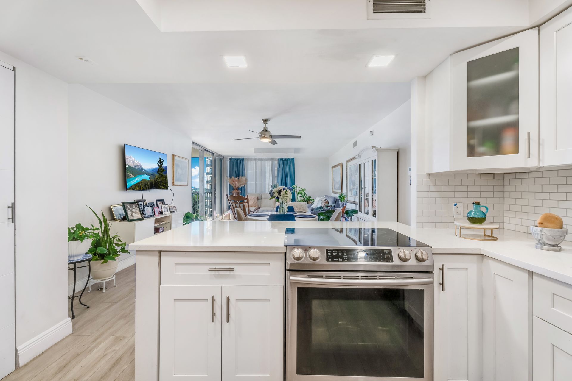 Bright, modern kitchen with white cabinets, a stainless steel oven, and an open floor plan leading to a living area.
