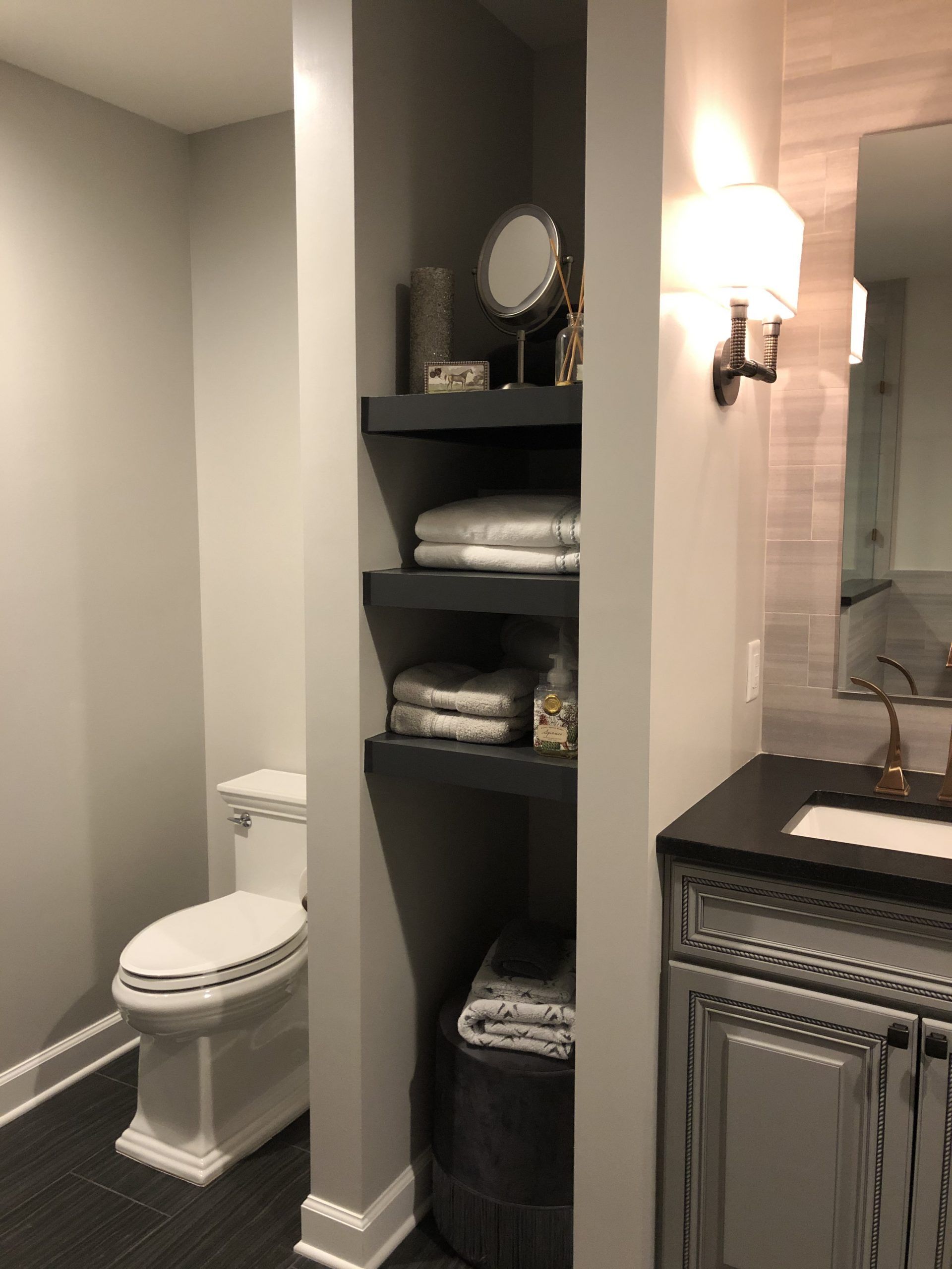 A bathroom with a toilet , sink , mirror and shelves.
