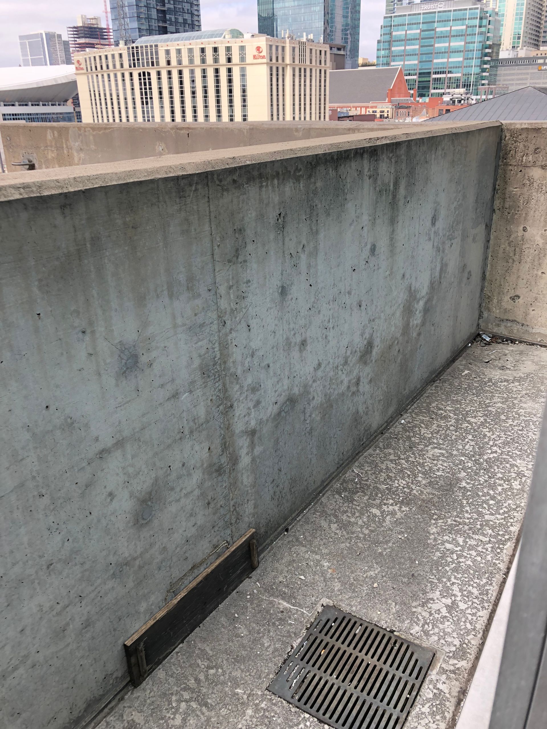 A concrete wall with a drain on it and a city in the background.