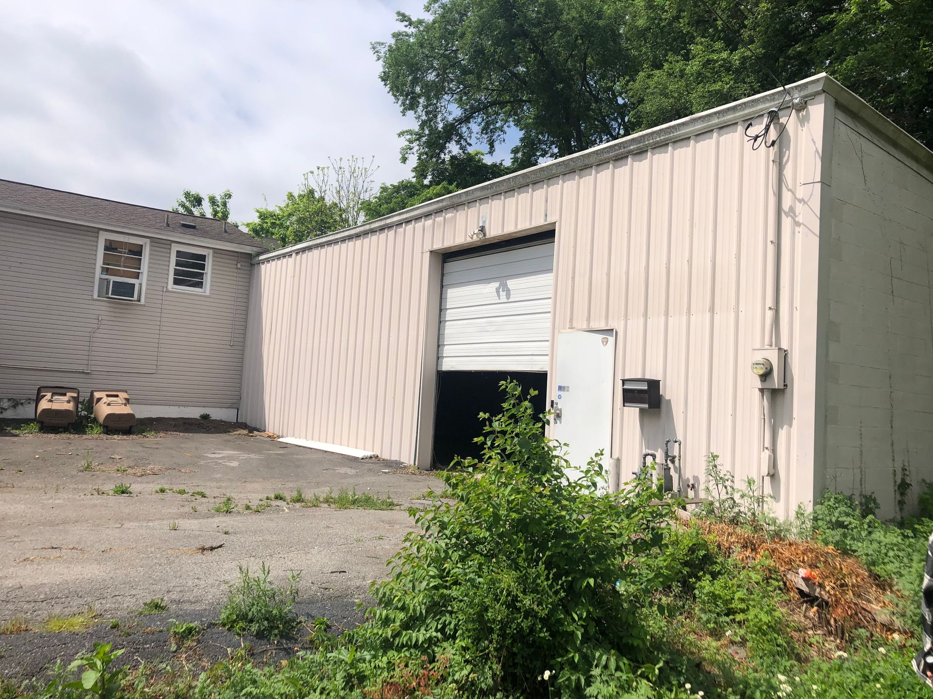 A white building with a white garage door is surrounded by trees.