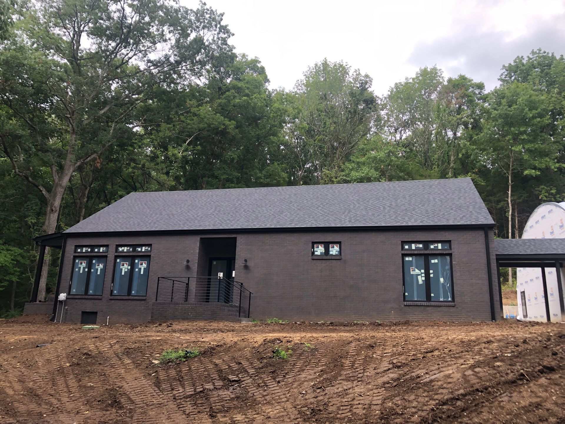 A black brick house is sitting on top of a dirt hill surrounded by trees.
