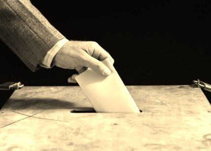 Image of man's hands placing a ballot in a ballot box.