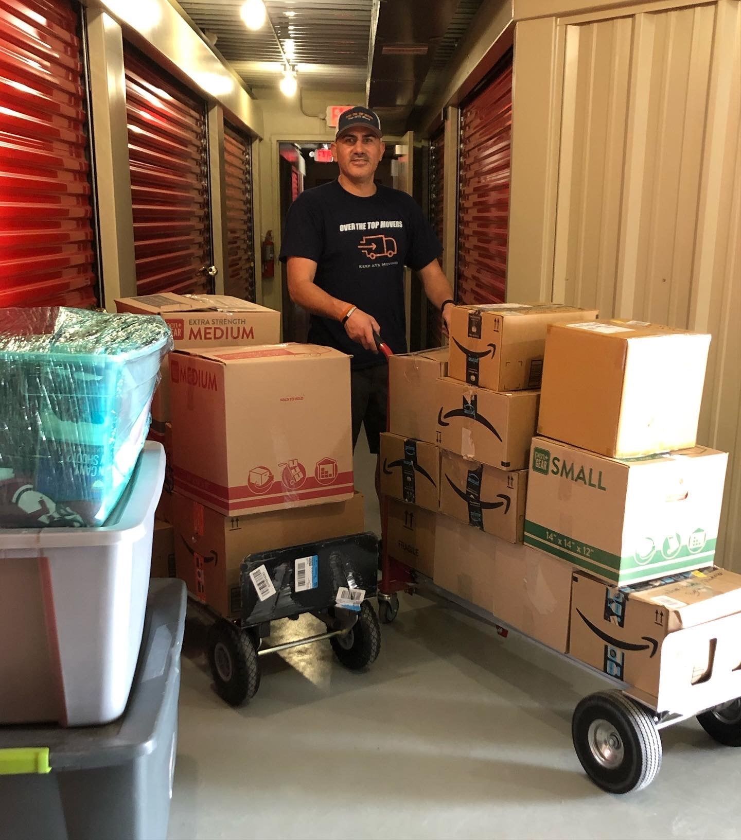 A man is pushing a cart full of boxes in a storage unit.