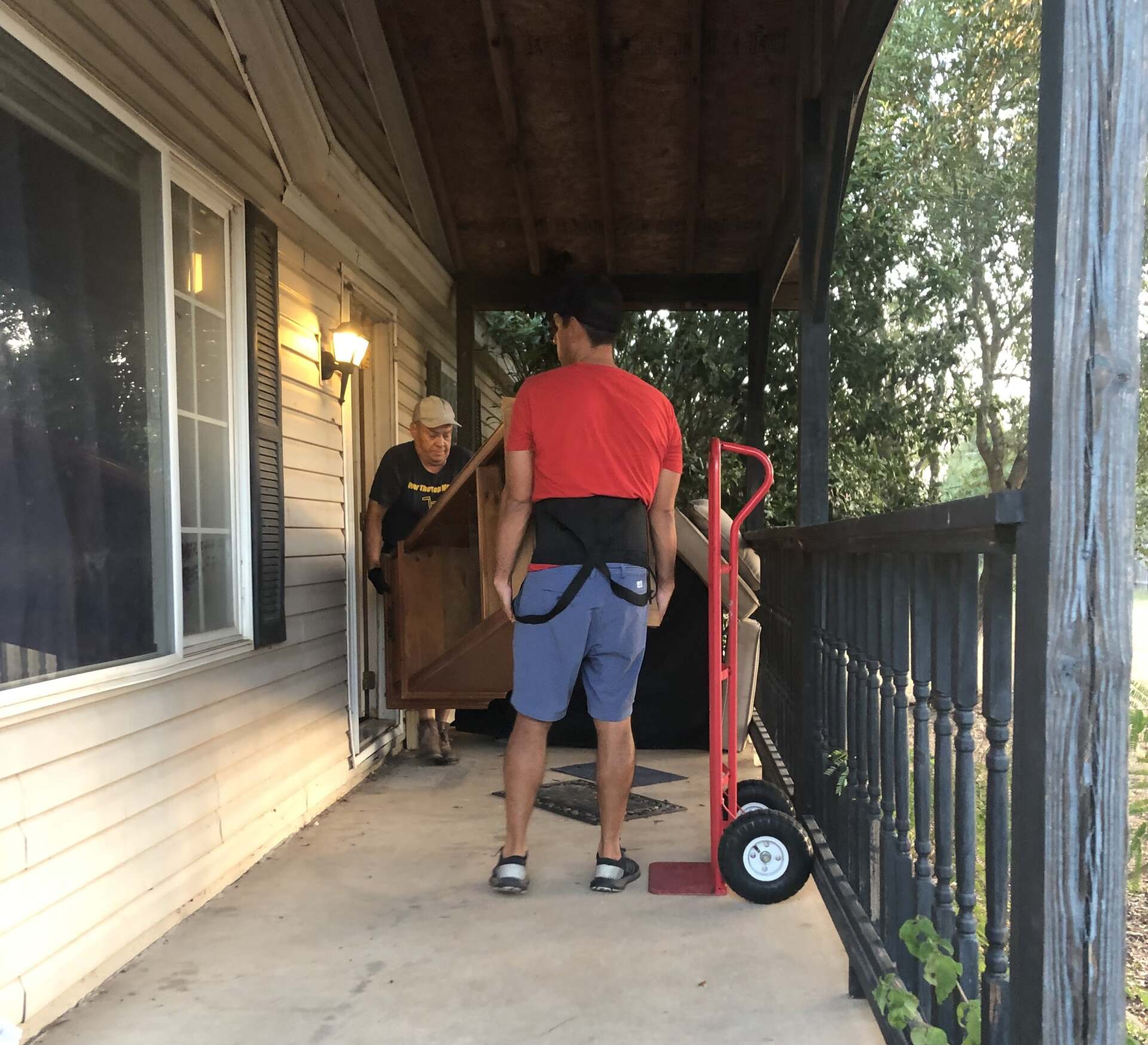 A man in a red shirt is carrying a piano on a dolly