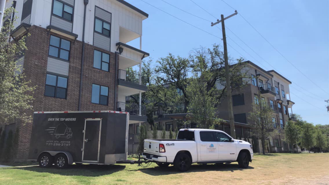 A white truck is parked in front of a building with a trailer attached to it.