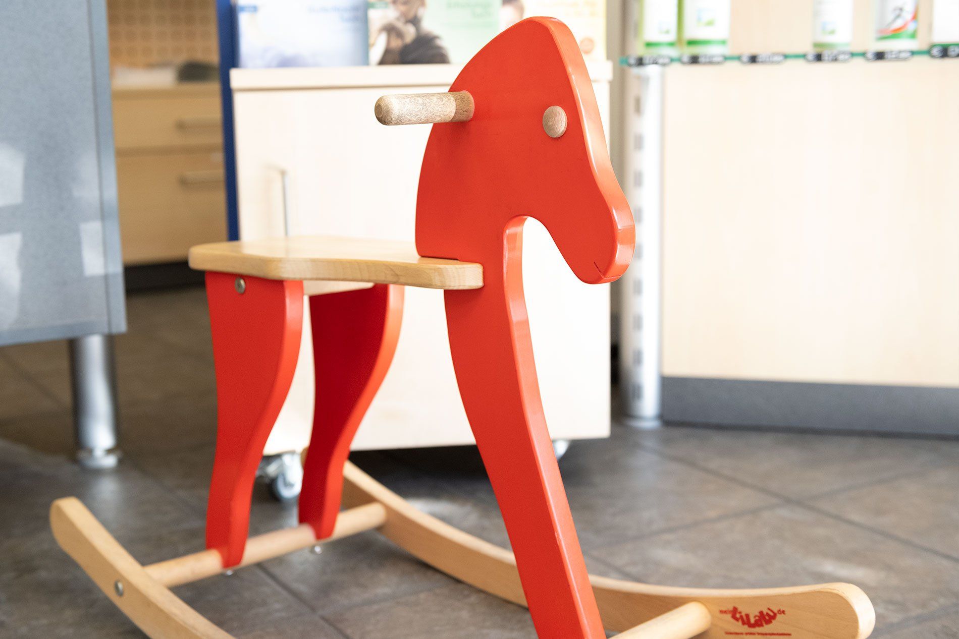 Ein rotes Schaukelpferd aus Holz sitzt auf einem gefliesten Boden