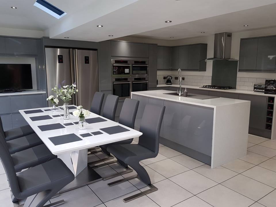 The same  large, modern, newly-fitted kitchen from the reverse angle, with an 8-seater modern dining table in the foreground.